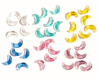 May include: Assortment of crescent moon shaped glass beads in various colours, including clear, light blue, pink, and yellow.