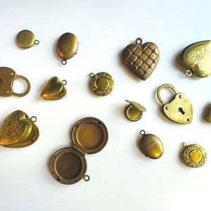 May include: A collection of brass-toned metal lockets and padlocks in various shapes including hearts, ovals, and circles. Some pieces are solid, while others are open to reveal interior compartments. Each item features a small loop for attachment.