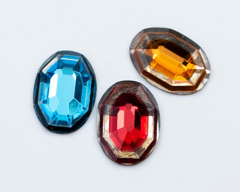 May include: Three oval-shaped, faceted glass gems with metal frames. The gems are blue, red, and orange.