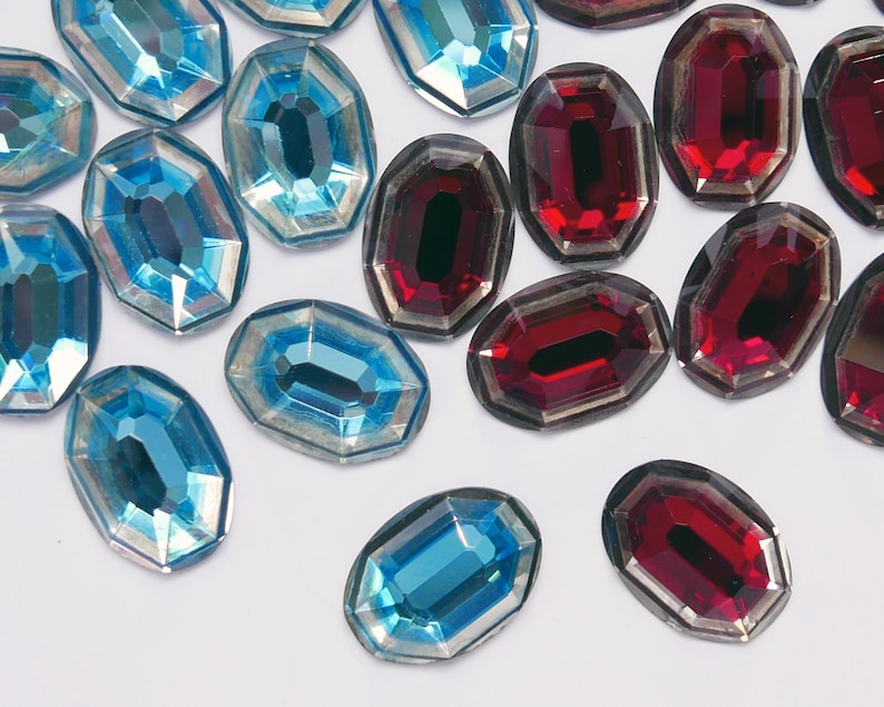 May include: Assortment of oval-shaped, faceted glass rhinestones in shades of blue and red. The rhinestones have a silver-toned backing.