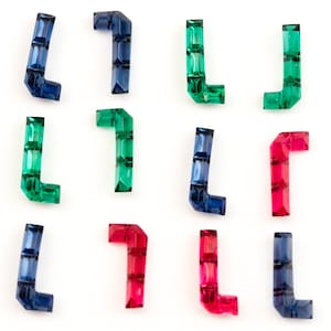 Puede incluir: Doce pequeños abalorios de cristal facetado en forma de letra L en tres colores: azul, verde y rojo. Los abalorios están dispuestos en tres filas de cuatro.