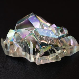 Könnte beinhalten: Ein Cluster aus irisierenden, klaren Quarzkristallen mit einem Regenbogen-Schimmer. Die Kristalle sind in einer zufälligen, organischen Form angeordnet.