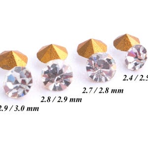 May include: Four clear glass rhinestones of varying sizes, with gold settings. The rhinestones measure 2.4/2.5 mm, 2.7/2.8 mm, 2.8/2.9 mm, and 2.9/3.0 mm.