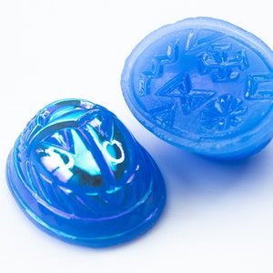 May include: Two blue glass scarab beetle charms, one with an iridescent finish and the other with a carved design.