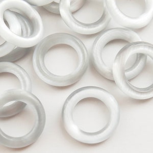Puede incluir: Un conjunto de cuentas circulares translúcidas, de color blanquecino. Las cuentas tienen forma de anillo con una superficie lisa y pulida. La iluminación crea reflejos y sombras, dándoles un brillo sutil. Adecuado para la creación de joyas.