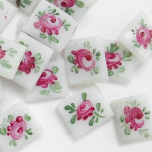 Könnte beinhalten: Eine Sammlung weißer Keramikfliesen mit handbemalten rosa Rosen und grünen Blättern.