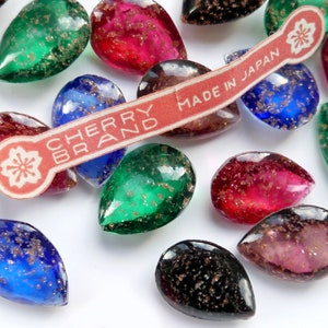 May include: Assortment of pearlescent glass teardrop shapes with gold flecks. The teardrops are in various colours, including green, red, blue, black, and purple. A label reads "Cherry Brand Made in Japan".