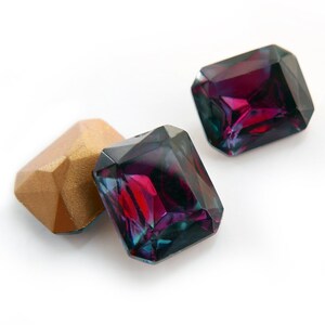 May include: Three faceted gemstones, two are dark purple with a green iridescent sheen and one is gold.