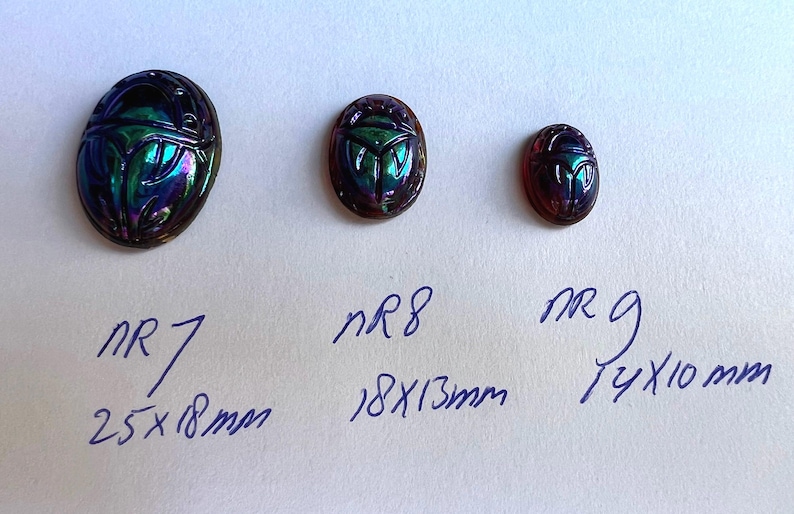 May include: Three iridescent glass scarab beetle cabochons in different sizes. The largest measures 2.5 inches by 1.8 inches, the middle measures 1.8 inches by 1.3 inches, and the smallest measures 1.4 inches by 1.0 inches.