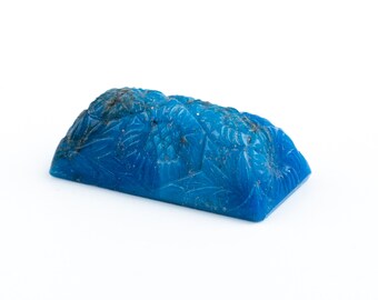 May include: A carved blue stone with a detailed floral design. The stone is rectangular and has a slightly curved top.