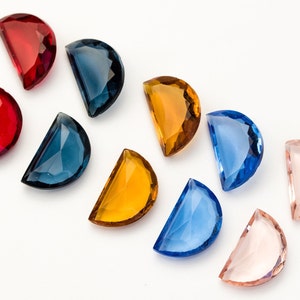 Puede incluir: Surtido de diez gemas de vidrio en forma de media luna en varios colores, incluyendo rojo, azul, amarillo y rosa. Las gemas están dispuestas en un semicírculo sobre un fondo blanco.