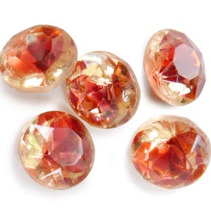 May include: Five round, faceted, iridescent glass gems in shades of red, orange, and gold. The gems have a shiny, reflective surface.