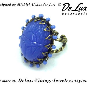 May include: A blue glass ring with a carved design, set in a brass bezel with a twisted wire band and blue beads around the edge.