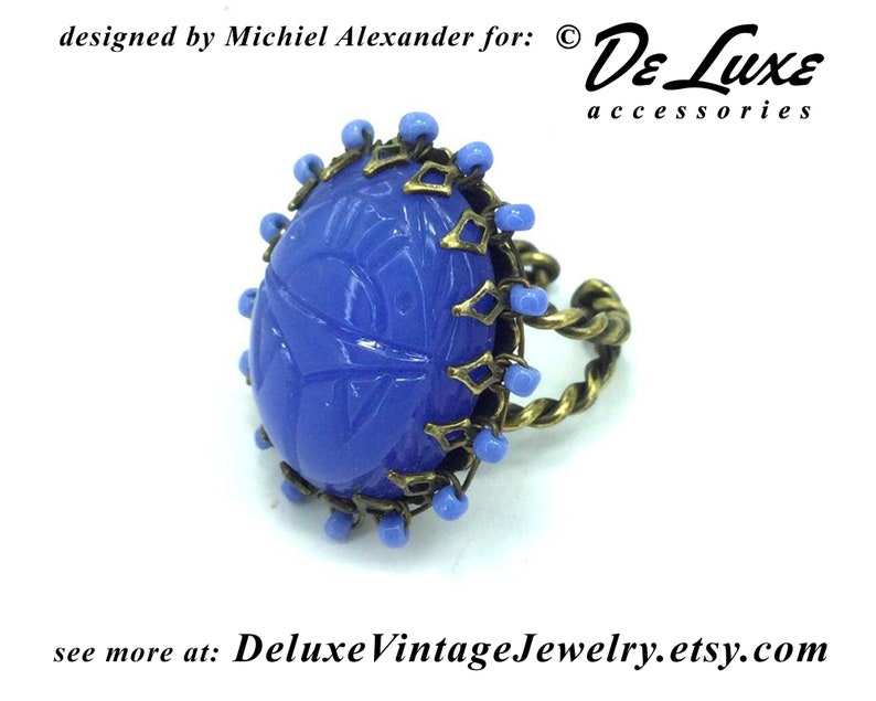 May include: A blue glass ring with a carved design, set in a brass bezel with a twisted wire band and blue beads around the edge.