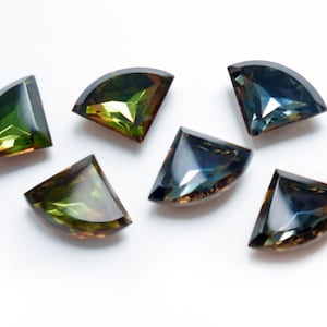 Puede incluir: Seis cabujones de piedras preciosas en forma triangular con un borde redondeado. Las piedras preciosas son una mezcla de verde y azul con un tono marrón.