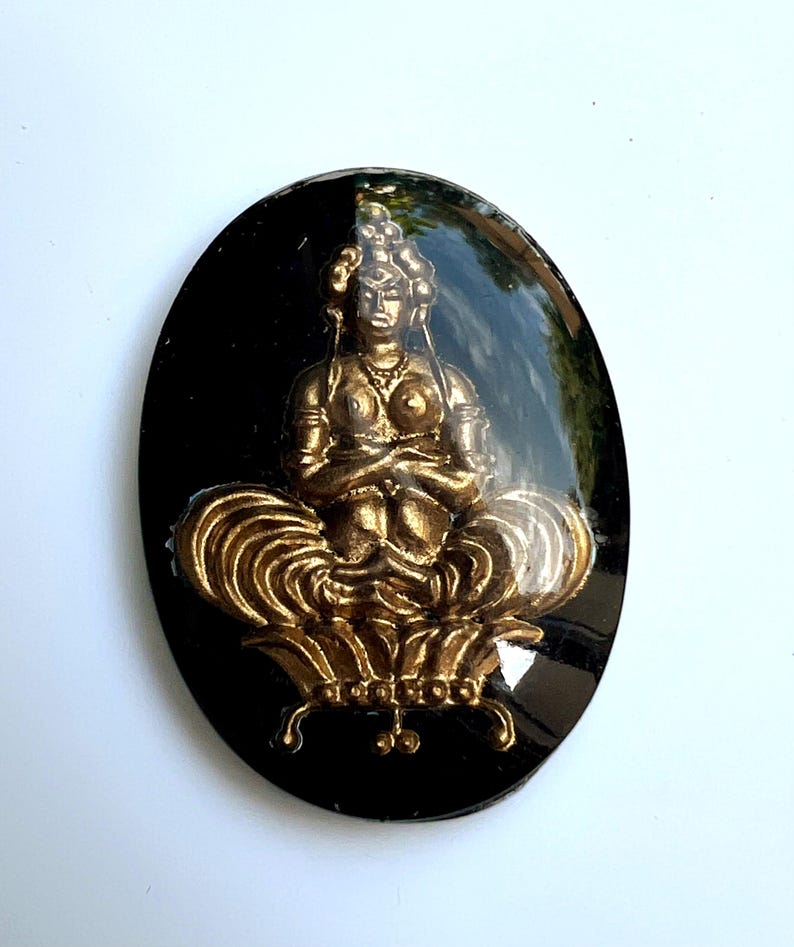 May include: An oval black resin pendant with a gold-coloured seated Buddha figure. The Buddha is in a meditative pose on a lotus flower. The pendant has a glossy finish, and the Buddha figure has intricate details.