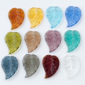 May include: Assortment of 12 glass leaf charms in various colors, including clear, blue, green, brown, red, and yellow. Each charm features a detailed leaf design.