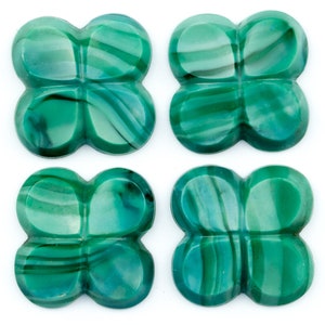Może przedstawiać: Cztery zielone kaboszony z malachitu w kształcie koniczyny czteroliściennej. Kaboszony mają wirujący wzór zielonego i ciemnozielonego.