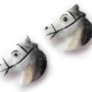 Puede incluir: Dos figuras de cabeza de caballo. Las cabezas son blancas con detalles en negro y gris, incluyendo bridas y crines. Las figuras probablemente est&aacute;n hechas de cer&aacute;mica o un material similar, y est&aacute;n sobre un fondo blanco.