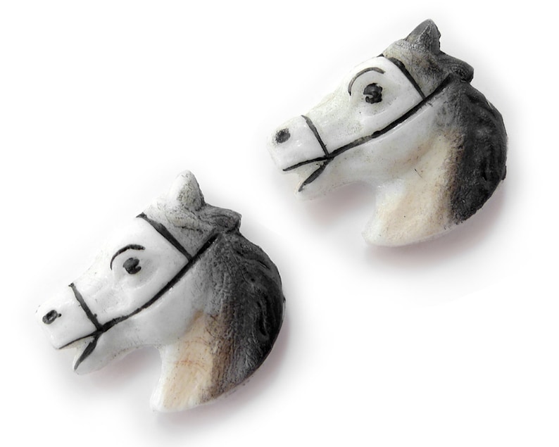 Puede incluir: Dos figuras de cabeza de caballo. Las cabezas son blancas con detalles en negro y gris, incluyendo bridas y crines. Las figuras probablemente est&aacute;n hechas de cer&aacute;mica o un material similar, y est&aacute;n sobre un fondo blanco.
