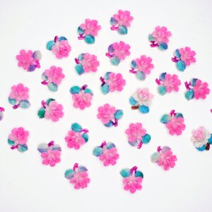 May include: A collection of pink and blue flower embellishments with a white background. The flowers are made of plastic and have a 3D effect.