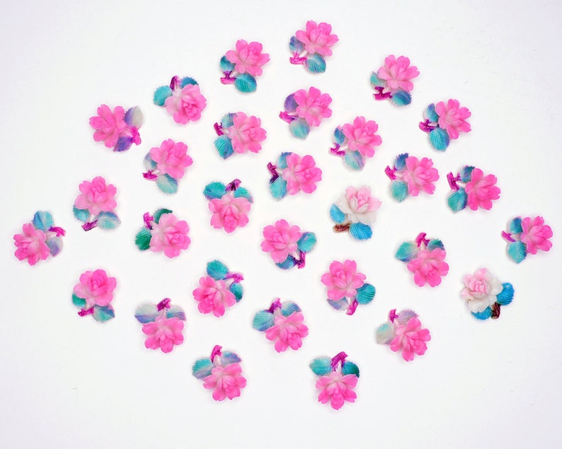May include: A collection of pink and blue flower embellishments with a white background. The flowers are made of plastic and have a 3D effect.
