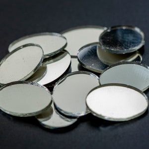 Op de afbeelding: Een stapel kleine, ronde, zilverkleurige spiegels op een zwart oppervlak.
