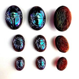 May include: Nine iridescent glass scarab beetle charms in various sizes. The beetles are a mix of blue, purple, and green with a metallic sheen. Some of the beetles have a red-brown color.
