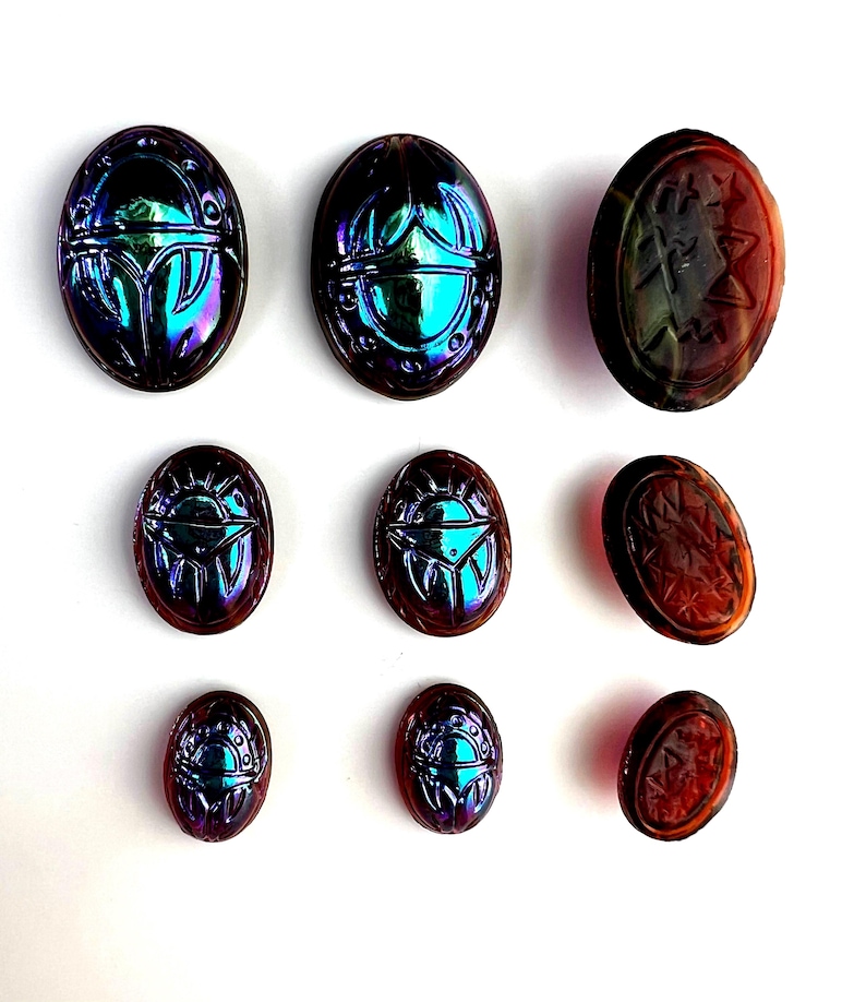 May include: Nine iridescent glass scarab beetle charms in various sizes. The beetles are a mix of blue, purple, and green with a metallic sheen. Some of the beetles have a red-brown color.