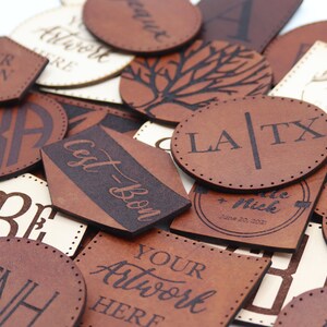 May include: A collection of brown leather labels with various designs and text, including "Your Design Here!" "Cest-Bon", "LA/TX", "FNH", and "Coffee".
