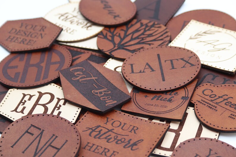 May include: A collection of brown leather labels with various designs and text, including "Your Design Here!" "Cest-Bon", "LA/TX", "FNH", and "Coffee".