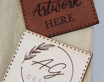 May include: Two leather labels with stitched edges. The top label is brown and says "YOUR Artwork HERE". The bottom label is cream colored and has a circle with a floral design and the text "A.G. DESIGN".