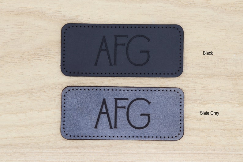 May include: Two leather labels with the initials "AFG" embossed in black. The top label is black and the bottom label is slate gray.