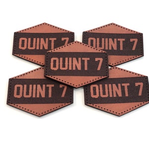 May include: Five brown leather patches with a stitched border and the text "QUINT 7" in white lettering.