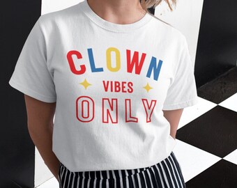 May include: A white short-sleeved t-shirt featuring the text CLOWN VIBES ONLY in red, yellow, and blue lettering. The word CLOWN is printed in a mix of red, yellow, and blue, while VIBES and ONLY are in red, accented by two yellow stars.