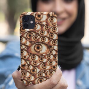 Pode incluir: Uma capa de telefone com um padrão de muitos olhos castanhos. A capa é feita de um material plástico rígido e tem uma borda elevada ao redor da lente da câmera para protegê-la de arranhões.
