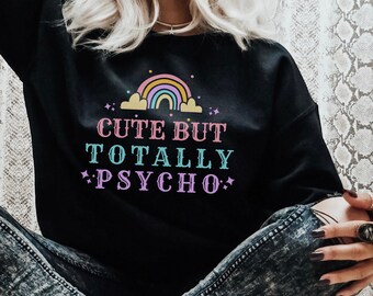 May include: Black sweatshirt with the text "Cute But Totally Psycho" in pink, teal, and purple. The design includes a rainbow and stars. The person is wearing ripped jeans and leopard print sneakers.
