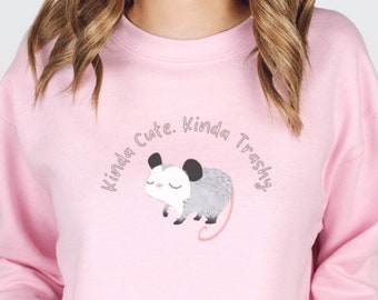 May include: A pink sweatshirt featuring a possum graphic and the text "Kinda Cute. Kinda Trashy."