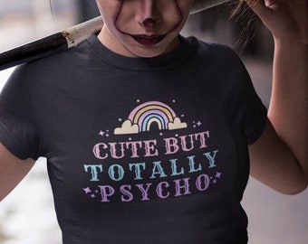 May include: A dark gray t-shirt with a rainbow, clouds, and the text "Cute But Totally Psycho" in pink, blue, and white.