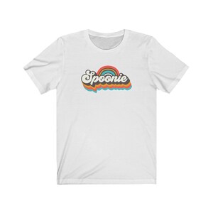 Op de afbeelding: Wit T-shirt met een retro-stijl grafische afbeelding met de tekst "Spoonie" in een regenboogkleurenschema.