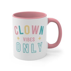 Puede incluir: Taza de cer&aacute;mica blanca con borde y asa de color rosa. La taza tiene el texto "CLOWN VIBES ONLY" en letras de colores.