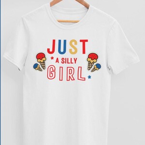 May include: White t-shirt with the text "JUST A SILLY GIRL" in colorful letters and ice cream cone graphics.
