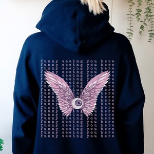 May include: A navy blue hoodie with a pink and white eye with wings on the back. The text "funny seeing you here" is repeated multiple times on the back of the hoodie.