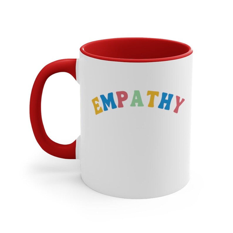 May include: White ceramic mug with a red rim. The mug has the word "EMPATHY" written in colorful letters.