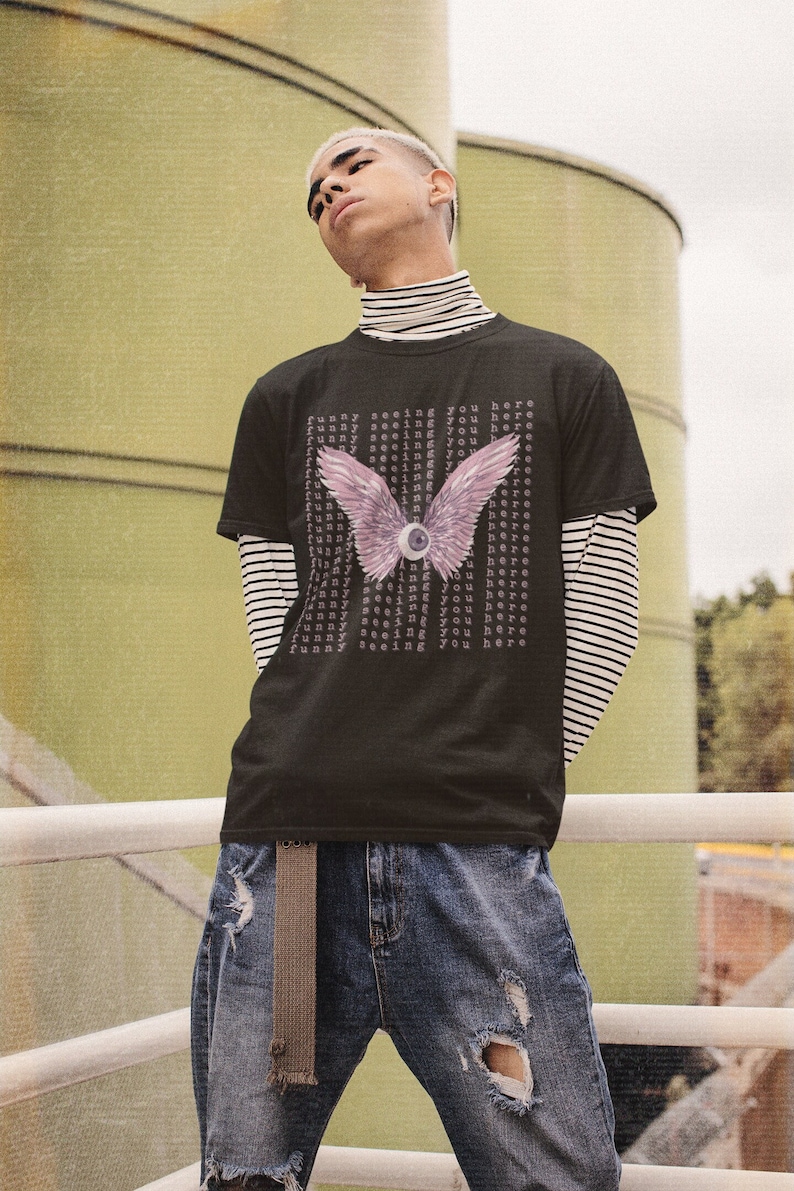 May include: Black t-shirt with a graphic of a pink eye with wings and the text "funny seeing you here" repeated multiple times.