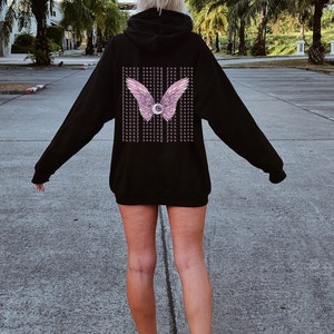 May include: Black hooded sweatshirt with a pink eye and wings graphic on the back. The graphic has the text "Funny seeing you here" repeated multiple times.