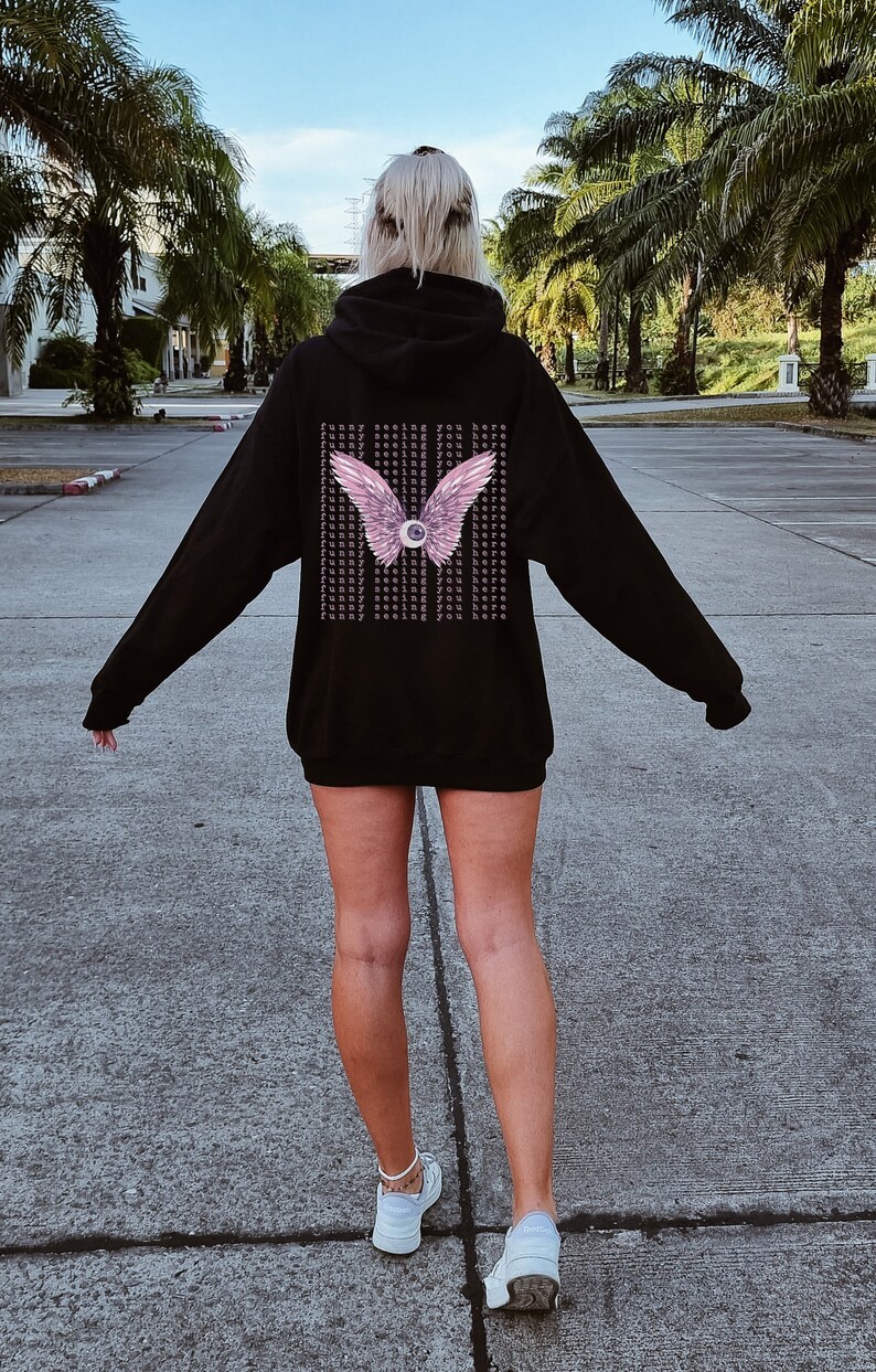 May include: Black hooded sweatshirt with a pink eye and wings graphic on the back. The graphic has the text "Funny seeing you here" repeated multiple times.