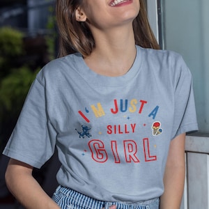May include: A light blue t-shirt with the text "I'm just a silly girl" in colorful letters. The shirt features a small graphic of a dog and an ice cream cone.