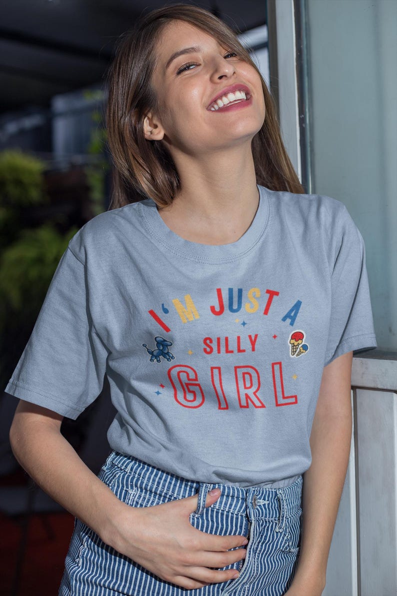 May include: A light blue t-shirt with the text "I'm just a silly girl" in colorful letters. The shirt features a small graphic of a dog and an ice cream cone.