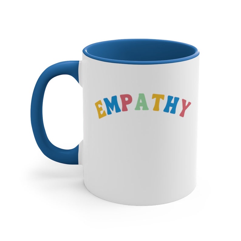 May include: White ceramic mug with a blue rim and handle. The mug has the word "EMPATHY" written in rainbow colors.
